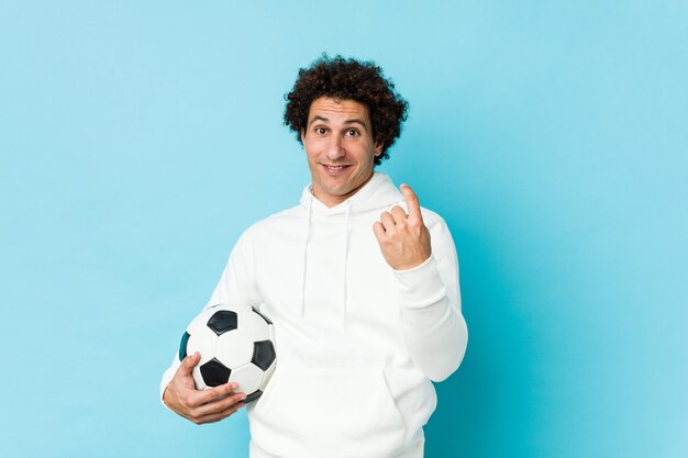 Uomo sportivo che tiene un pallone da calcio che punta con il dito contro di te come se l'invito si avvicina.