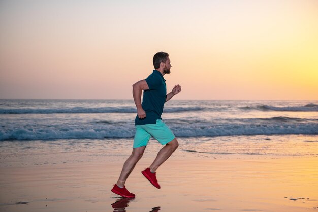 Uomo sportivo corridore in esecuzione in estate spiaggia colorato tramonto cielo