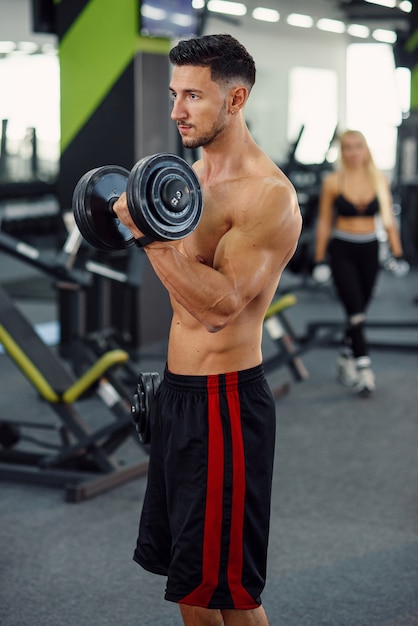 Uomo sportivo fitness facendo esercizi per bicipiti con manubri in palestra elegante