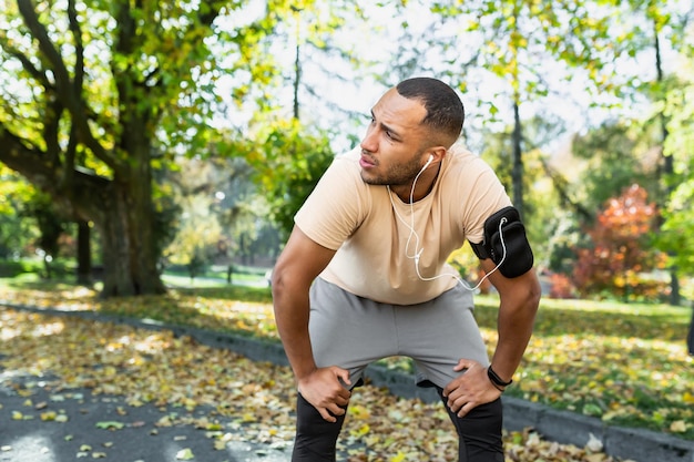 Uomo stanco che riposa nel parco dopo il jogging e la lezione di fitness uomo ispanico che usa l'ascolto del telefono