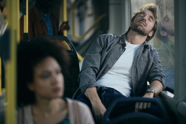 Uomo stanco che si appoggia su una finestra e dorme mentre si sposta in autobus