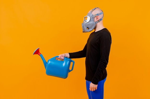 Uomo strano divertente in respiratore in posa con annaffiatoio blu su sfondo arancione