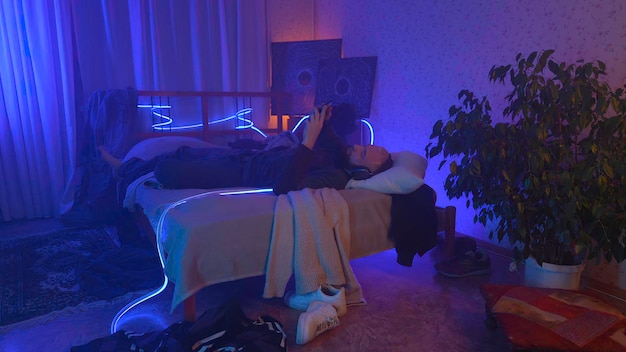 Uomo stressato sdraiato sul letto a casa mentre tiene la testa sullo sfondo al neon