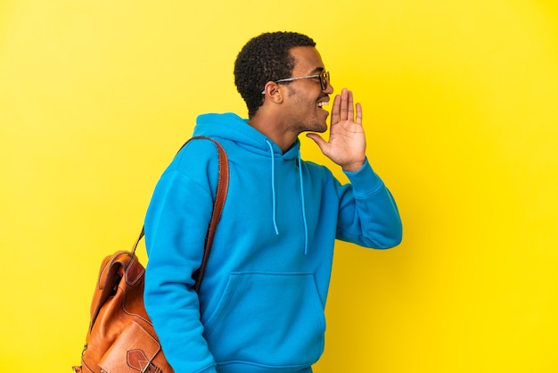 Uomo studente afroamericano su sfondo giallo isolato che grida con la bocca spalancata al laterale