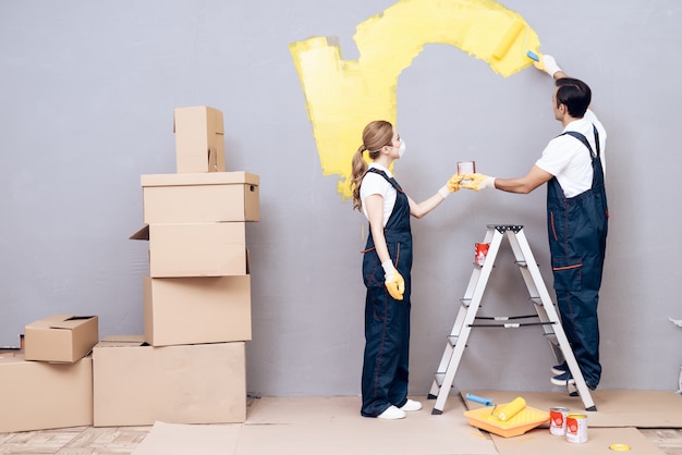 Uomo su etichetta e donna in uniforme dipingere parete grigia