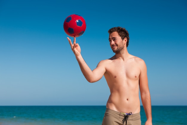 Uomo sul pallone da calcio d'equilibratura della spiaggia