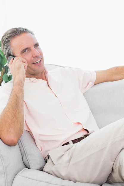 Uomo sul suo divano facendo telefonata sorridendo alla telecamera