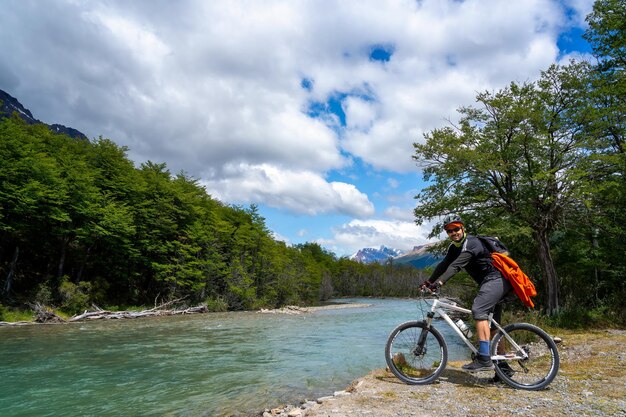 Uomo sulla bici nella foresta vicino al fiume con le montagne sullo sfondo