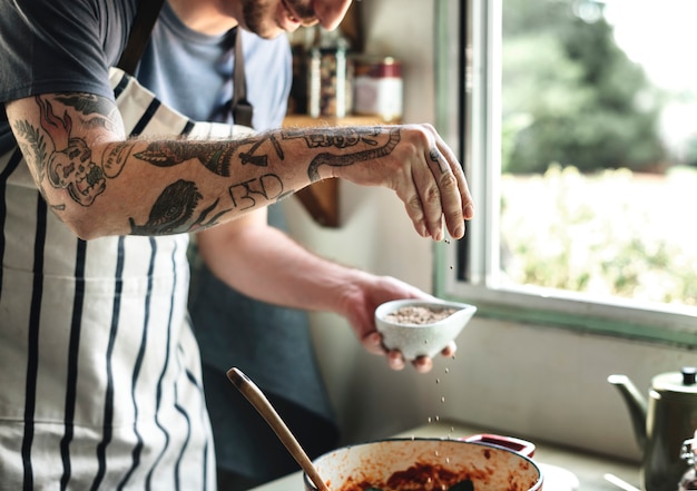 Uomo tatuato che cucina in una cucina di campagna