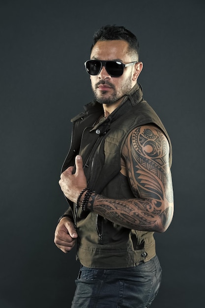 Uomo tatuato con bicipiti e tricipiti Modello tatuaggio con barba sul viso non rasato Uomo barbuto con tatuaggio su braccia forti Macho alla moda con occhiali da sole alla moda Stile moda e tendenza