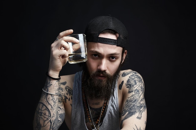 Uomo tatuato in cappello che beve un whisky