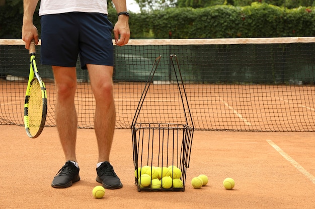 Uomo tenere la racchetta sul campo in terra battuta con cesto di palline da tennis