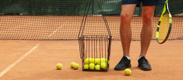 Uomo tenere la racchetta sul campo in terra battuta con cesto di palline da tennis