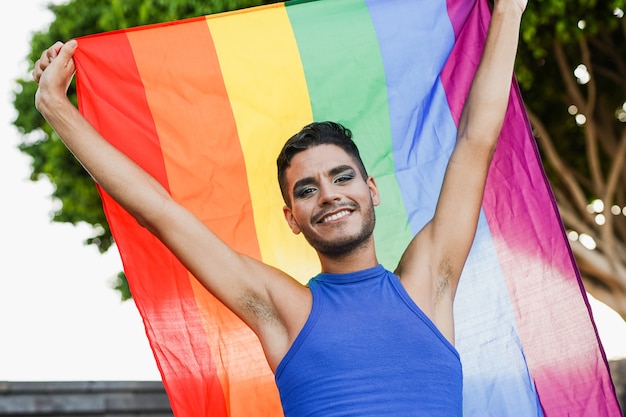 Uomo transgender con trucco che tiene bandiera arcobaleno lgbt in città - concetto LGBTQIA