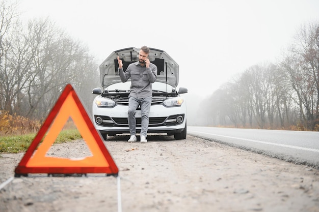 Uomo triste sulla strada accanto alla macchina rotta