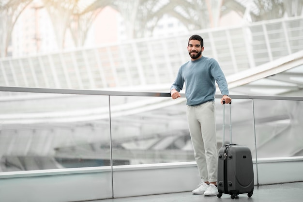 Uomo turistico felice che posa con la valigia di viaggio all'aeroporto moderno