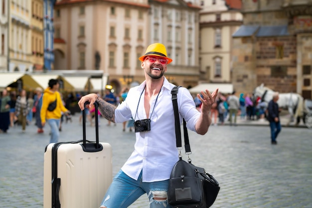 Uomo turistico in jeans cappello di moda e occhiali da sole con la valigia che cammina sul viaggiatore uomo di strada con su