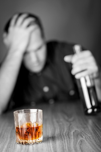 Uomo ubriaco e triste con bottiglia e bicchiere di liquore al bancone del bar