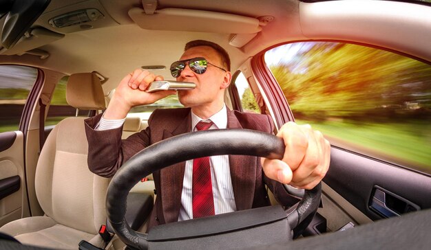 Uomo ubriaco in tuta e occhiali da sole che guida su una strada nel veicolo dell'auto.