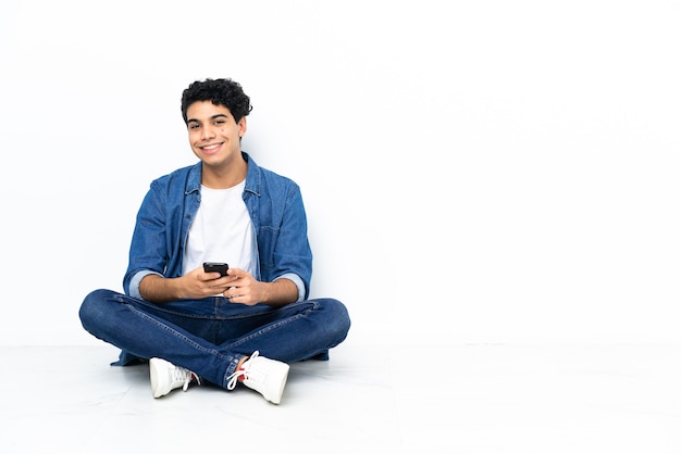 Uomo venezuelano seduto sul pavimento che invia un messaggio con il cellulare