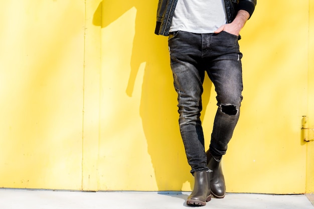 Uomo vestito con t-shirt bianca, giacca e jeans su sfondo giallo. Vista ravvicinata sulla vita senza volto