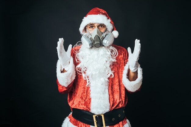 Uomo vestito da Babbo Natale che indossa una maschera con filtro a carbone per evitare di contrarre un virus, su sfondo nero. Concetto di Natale, Babbo Natale, regali, celebrazione.