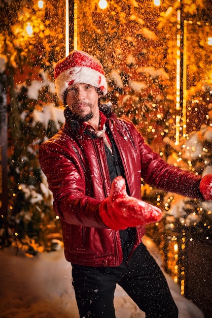 Uomo vestito da Babbo Natale vomita neve su una strada decorata con ghirlande concetto di Capodanno e Natale media misti