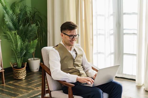 Uomo vestito in modo elegante che lavora al portatile in una stanza verde soleggiata