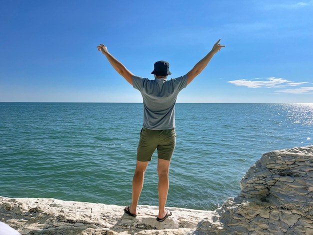 Uomo viaggiatore con le mani in alto godendo di una splendida vista sul mare dalla costa rocciosa