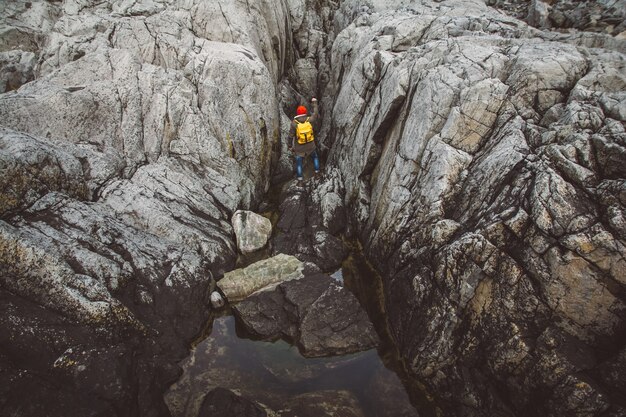 Uomo viaggiatore con uno zaino giallo che indossa un cappello rosso in piedi su uno sfondo di rocce