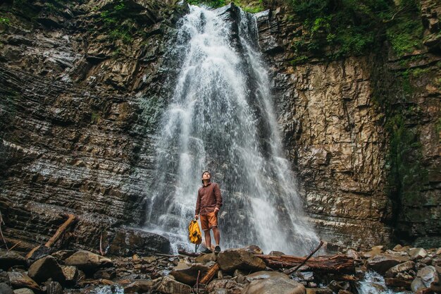 Uomo viaggiatore con uno zaino giallo in piedi sullo sfondo di una cascata