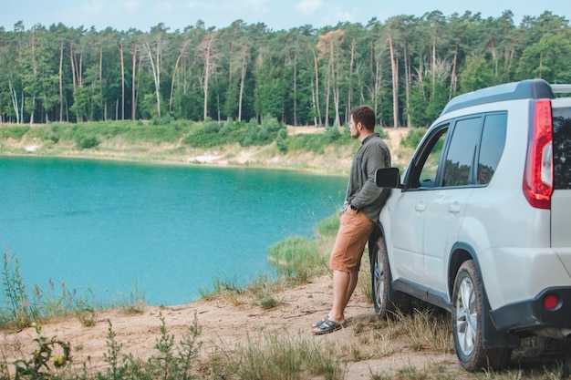 Uomo vicino a un'auto suv bianca sul bordo guardando il lago con acqua blu