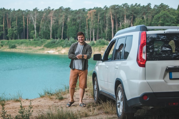 Uomo vicino a un'auto suv bianca sul bordo guardando il lago con acqua blu