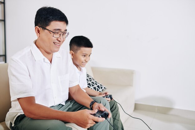 Uomo vietnamita maturo che si diverte a giocare al videogioco con suo figlio preadolescente a casa