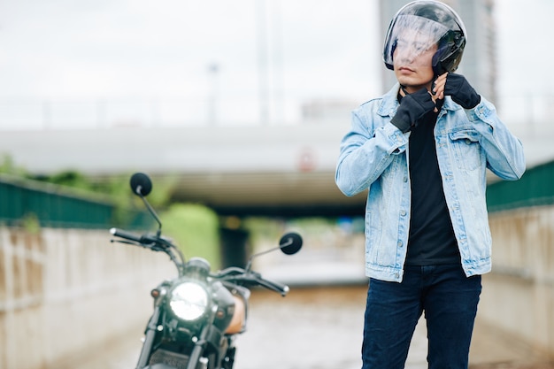 Uomo vietnamita serio fiducioso che allaccia il casco del motociclo prima del giro