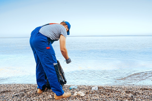 Uomo volontario in piedi sulla spiaggia con un sacco pieno di spazzatura raccolta