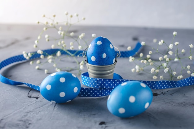Uova a pois blu brillante con un nastro e fiori primaverili bianchi su sfondo grigio Carta di Pasqua festiva