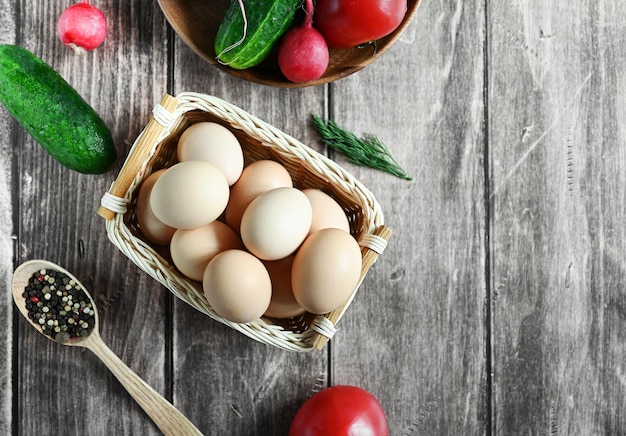 Uova beige fatte in casa fresche in un cestino e verdure su uno spazio della copia di vista superiore del tavolo di legno