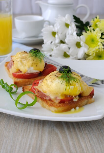 Uova Benedict con prosciutto e pomodoro e formaggio su pane tostato con succo d'arancia e caffè