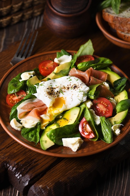 Uova Benedict (in camicia) con prosciutto di Parma, fette di avocado, pomodoro e foglie di spinaci teneri, condite con olio di oliva piccante aromatizzato