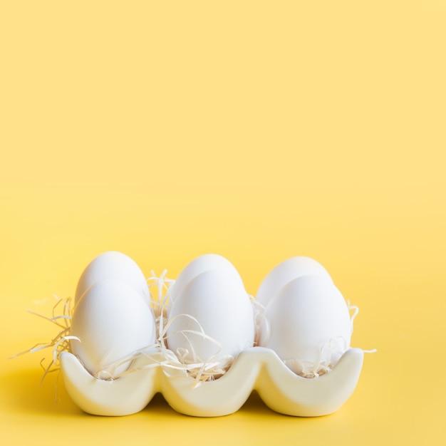 Uova bianche organiche del pollo in scatola decorativa della porcellana su giallo.