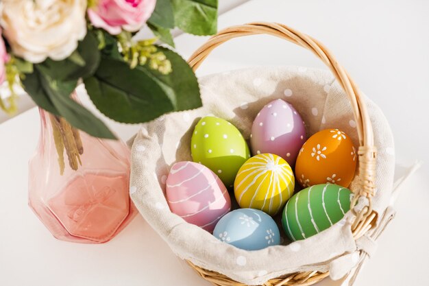 Uova colorate di Pasqua in busket bianco sulla tavola di legno. Bouquet di fiori di rosa sul tavolo. Buona Pasqua. Atmosfera primaverile.