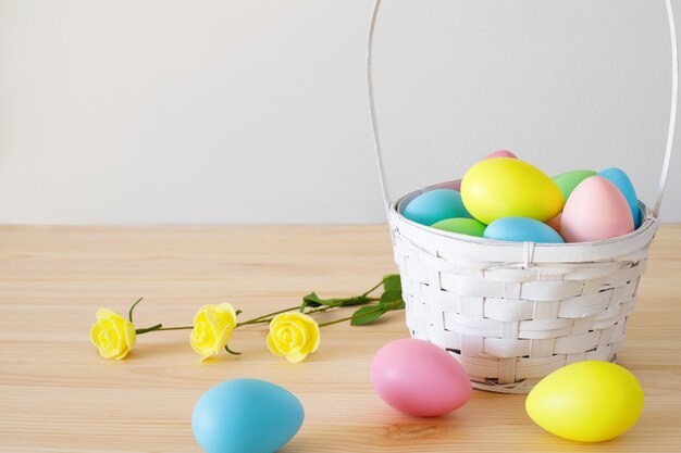 Uova colorate di Pasqua nel cesto e piccoli fiori sullo sfondo di un tavolo di legno