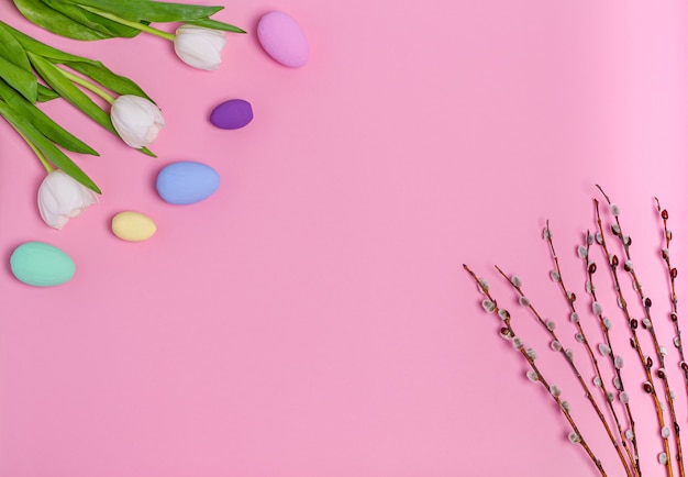 Uova colorate di Pasqua, un mazzo di tulipani bianchi e rami di salice su uno sfondo rosa, copia spazio