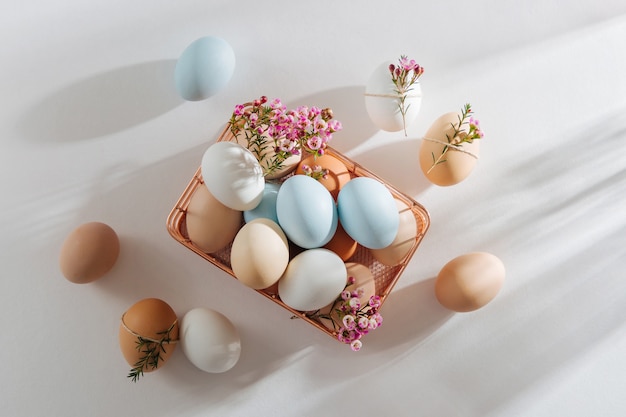 Uova colorate naturali e fiori nel cesto con i raggi del sole. Composizioni alla moda in colori pastello. Concetto di Pasqua.