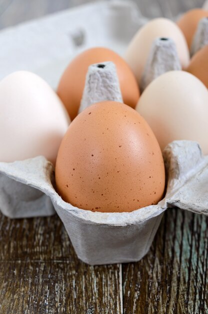 Uova crude fresche del pollo in scatola delle uova del cartone su fondo di legno. Vista del primo piano sulle uova marroni e bianche.