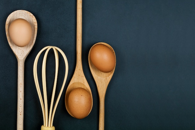 Uova, cucchiaio di legno e baffo. Utensile da cucina per torta, pasticceria o biscotti su sfondo di tabellone.