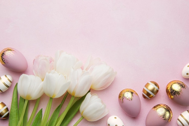 Uova d'oro di Pasqua e tulipani rosa su sfondo rosa