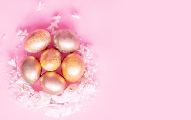 Uova d'oro in un nido di fiori su sfondo rosa Concetto di Pasqua con spazio per il testo