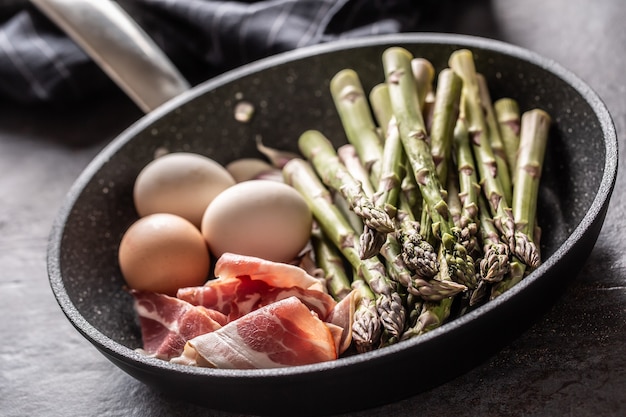 Uova di asparagi pancetta e aglio in padella in ceramica.